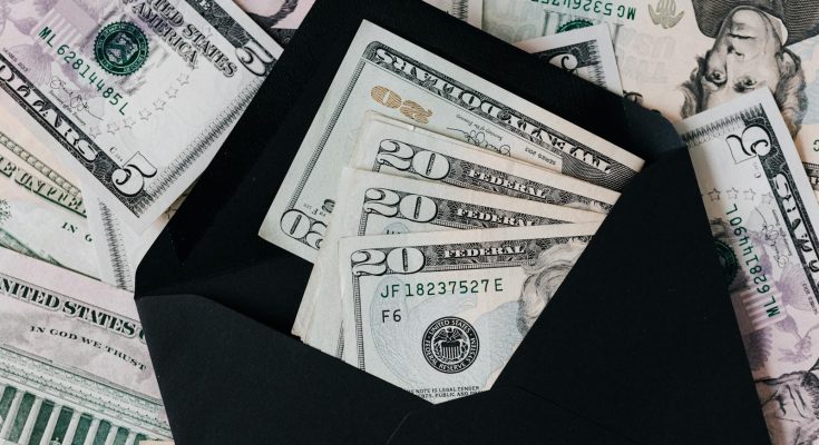 From above of dollar bills in opened black envelope placed on stack of United states cash money as concept of personal income